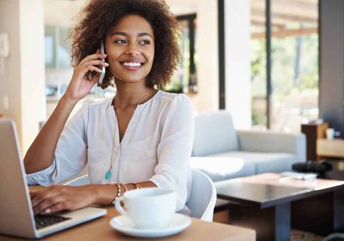 Shot of an attractive young woman working on a laptop at home while talking on her cellphone