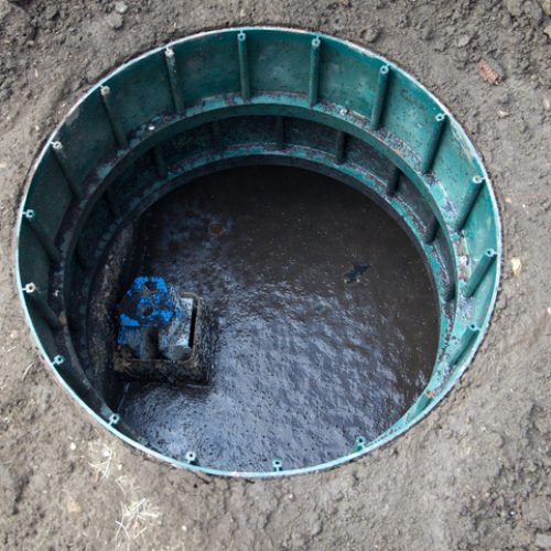 Overhead view of an open residential septic tank. Safety cover removed.Outlet filter screen visible.